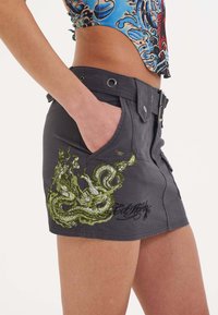 Grijze denim mini-jurk met groen dragontapijt, voorzakken en een decoratieve riemlus. Getextureerde stof met drukknoopjes.