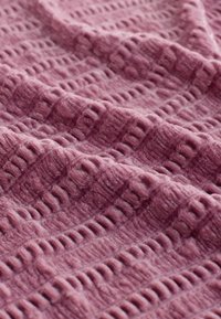 Gestructureerde deken in zacht mauve, met een verhoogd, patroonontwerp van horizontale en verticale lijnen, die een gezellige, weelderige uitstraling creëren.