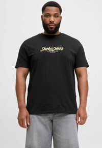 Fekete, rövid ujjú póló arany színű logóval, amelyen a "Jack & Jones World Wide Studio" felirat található, kerek nyakkivágással és sima textúrával.