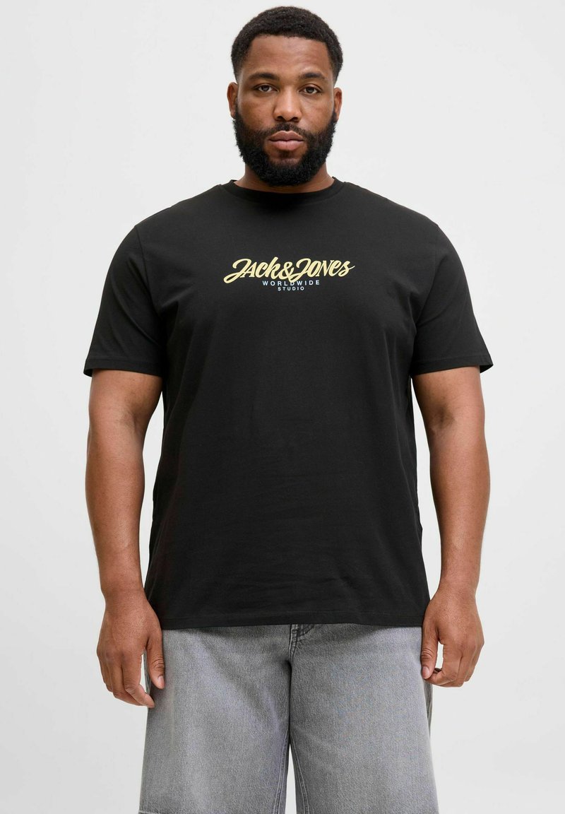 Fekete, rövid ujjú póló arany színű logóval, amelyen a "Jack & Jones World Wide Studio" felirat található, kerek nyakkivágással és sima textúrával.