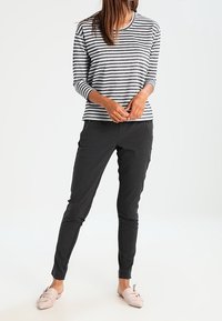 Striped long-sleeve top in black and white, paired with slim-fit black pants and light pink slip-ons featuring a bow detail.