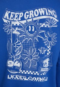 Tricou albastru cu grafica albă a florilor, a soarelui, a unui chip zâmbitor și a textului „CONTINUĂ SĂ CREȘTI” și „CONTINUĂ SĂ MERGI”, având modele și desene în grilă.