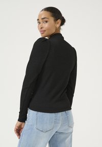 Black long-sleeve top with a textured fabric and a high neck. Features puffed shoulder accents, paired with light-wash denim jeans.