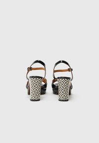 Μαύρα δερμάτινα σανδάλια με τακούνι και λουράκι στο αστράγαλο, με γεωμετρικό μοτίβο στο τετράγωνο τακούνι σε μαύρο και λευκό. Λείο υφή, μίνιμαλ σχεδιασμός.