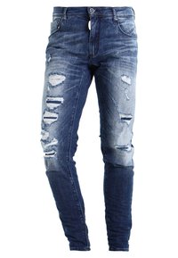 Vaqueros de mezclilla azul con múltiples roturas y desgastes intencionados en los muslos delanteros y las rodillas, estilo ajustado.