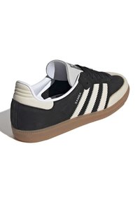 Black suede sneaker with white leather accents and three stripes. Gum rubber sole. Low top with padded collar and black laces.