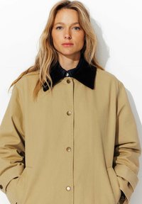 Veste d'extérieur khaki avec un col en velours côtelé, des boutons-pression et des poches latérales, présentant une texture lisse et une coupe décontractée.