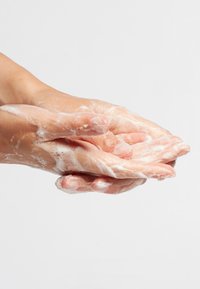 Handen met een lichte huidtint, bedekt met dikke witte zeepbellen, zijn samen geplaatst en benadrukken de wasbeweging op een lichte achtergrond.