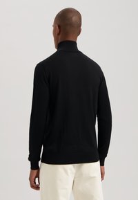 Pullover nero a maniche lunghe con colletto alto, caratterizzato da una texture liscia e un design aderente. Il modello è mostrato di spalle.