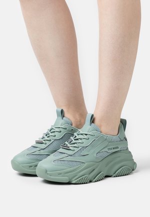 Lysegrønne chunky sneakers med meshpaneler og snørebånd, båret på bare fødder, med "Steve Madden"-branding på siden.
