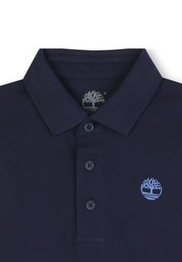Polo marine avec un col classique, trois boutons et un petit logo d'arbre bleu sur le côté gauche. Tissu texturé avec une finition côtelée.