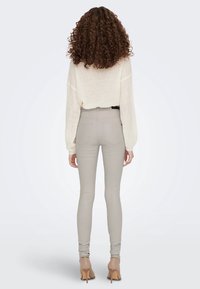 Lichtbeige skinny jeans gecombineerd met een losvallende witte gebreide trui, met een textuurdesign en een ronde halslijn.