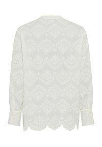 Weißes Blusenshirt mit langen Ärmeln, das ein strukturiertes Blumendesign, einen gewellten Saum und geknöpfte Manschetten aufweist. Leichter Stoff mit einer sanften Oberflächenbeschaffenheit.