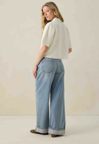 Witte textuur cropped top met een kraag, gecombineerd met lichtblauwe wide-leg jeans met opgerolde mouwen en een klassiek denim ontwerp.
