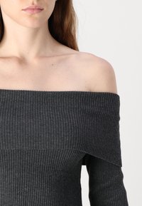 Sweater escuro cinza, canelado e off-the-shoulder, com um acabamento texturizado, apresentando um decote largo e um design em camadas no corpete.