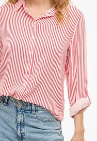 Chemise rayée rouge et blanche avec un col pointu, manches retroussées et un tissu doux, associée à un short en denim bleu taille haute.