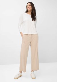 Witte blouse met lange mouwen, beige wijde broek en witte veterschoenen. Gladde stof, relaxte pasvorm en subtiele stiksels.
