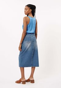 Denim midi-rok met een vervaagde blauwe tint, voorzien van een achterzak en een soepel, effen blauwe tanktop. Bruine open hakschoenen maken de look compleet.