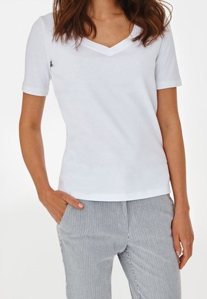 Camiseta blanca de cuello en V y mangas cortas, hecha de una tela suave. Combinada con pantalones a medida a rayas con un patrón en azul claro y blanco.