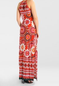 Vestido maxi de un rojo brillante con estampados florales, con cuello halter, corsé ajustado y dobladillo acampanado. Telas suaves con detalles vibrantes.