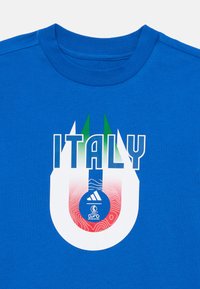 Camiseta de algodón azul con la palabra "ITALIA" en letras blancas en negrita, acentos verdes y un logo circular gráfico con patrones de olas rojas.
