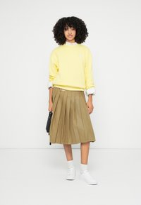 Żółta bluza z prążkowanymi mankietami, zestawiona z khaki plisowaną spódnicą i białymi trampkami. Stylizację uzupełnia czarna torba na ramię.