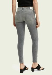 Pantalones de mezclilla gris delgado, de cintura media, diseño de cinco bolsillos, detalle de yugo trasero, combinados con sandalias negras de tacón. Textura suave, forma ajustada.