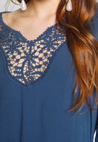 Dunkelbluse mit kunstvollen Spitzendetails am Ausschnitt, aus einem weichen und leicht strukturierten Stoff mit einem V-Ausschnitt.