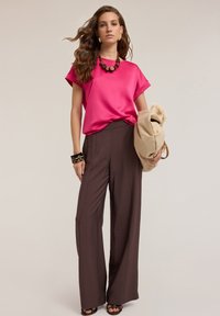 Fuchsia satin topp med rullade ärmar, parat med bruna vida byxor. Accessoarer inkluderar ett kraftigt brunt halsband och en texturerad beige väska.