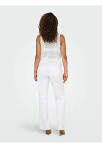 Witte kanten mouwloze top met een geometrisch patroon, gecombineerd met witte wijde broekspijpen en bruine hoge hakken. Zicht vanuit de achterkant.