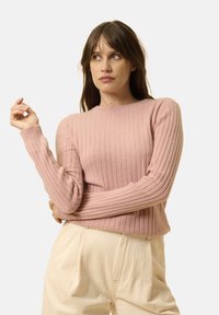 Suéter de punto acanalado de color rosa claro con mangas largas y escote redondo, combinado con pantalones holgados de color crema. Textura suave y diseño ajustado.