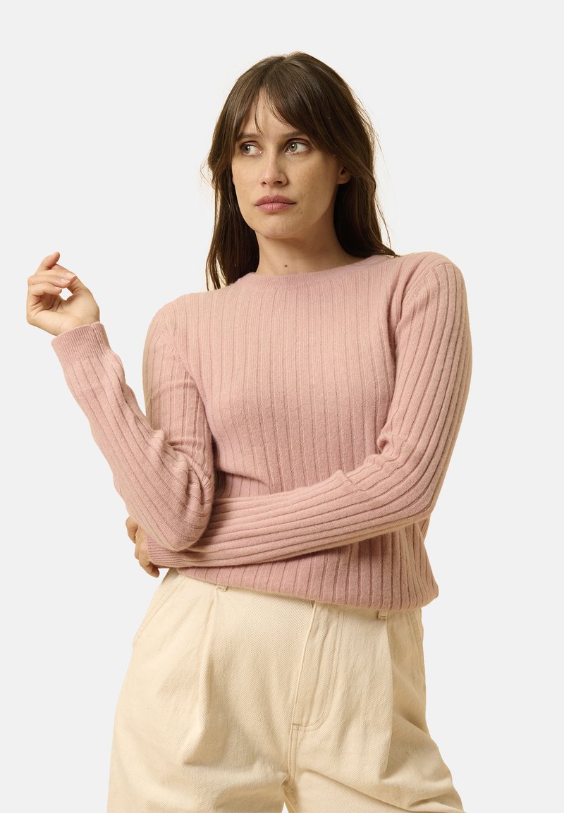 Suéter de punto acanalado de color rosa claro con mangas largas y escote redondo, combinado con pantalones holgados de color crema. Textura suave y diseño ajustado.