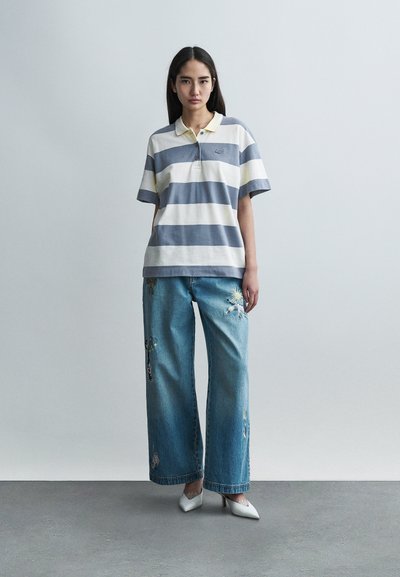 Polo rayé gris et blanc avec des accents jaunes, assorti à un jean en denim à jambes larges orné de broderies florales et d'un lavage clair.