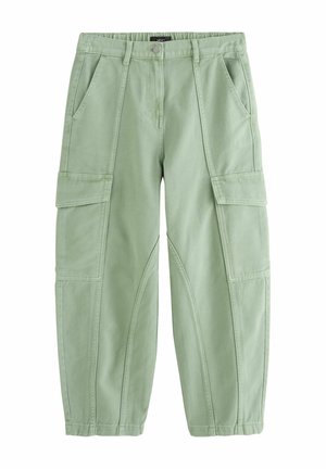 Personne portant un pantalon cargo vert clair avec de grandes poches à l’arrière et sur les côtés, un haut sans manches rayé, une montre et des sandales compensées marron, debout devant un fond beige.