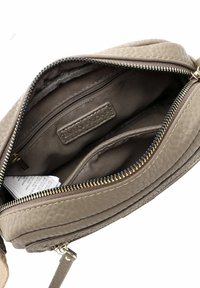 Intérieur d'un sac en cuir marron texturé avec plusieurs compartiments, fermeture éclair, doublure en tissu et étiquette de marque.