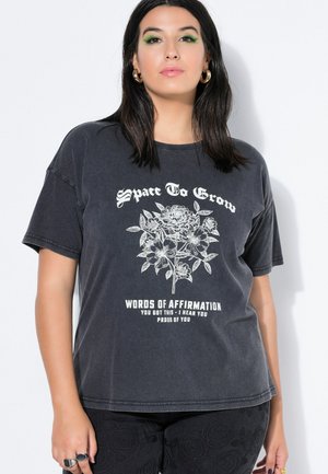 Kobieta o ciemnych włosach ubrana w czarną koszulkę z białą kwiatową ilustracją i napisem „Space To Grow” oraz afirmacjami poniżej.