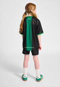 Zwart sportshirt met groene accenten, zwarte shorts en groene schoenen. Shirt heeft een verticale groene streep en de tekst "INTERNATIONALS".