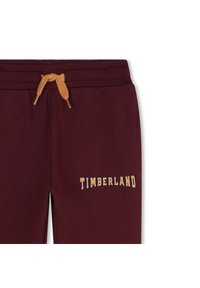 Pantalons de survêtement bordeaux avec une taille élastique, dotés d'un cordon de serrage jaune et d'un logo "TIMBERLAND" en lettres courbes sur le côté.