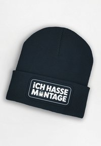 Navy knitted beanie with a ribbed texture. Features a white patch with the text "ICH HASSE MONTAGE" and an illustration of a character.