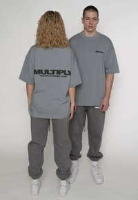 Grå oversize t-shirts med sort "MULTIPLY" print på bagsiden, parret med grå joggingbukser og hvide sneakers. Blødt bomuldsmateriale.