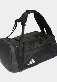Sac de sport noir en tissu résistant, avec un compartiment principal zippé, des sangles réglables et des accents de logo blancs.