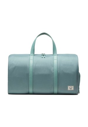Sac de sport cylindrique bleu clair avec deux poignées et fermeture à glissière, présentant un petit patch rectangulaire avec le logo Herschel en bas à droite.