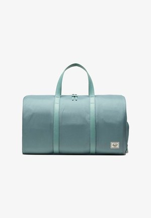 Sac de sport cylindrique bleu clair avec deux poignées et fermeture à glissière, présentant un petit patch rectangulaire avec le logo Herschel en bas à droite.