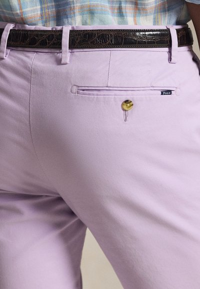 Κοντινή λήψη λιλά παντελονιού με μαύρη δερμάτινη ζώνη, μια κουμπωμένη πίσω τσέπη και μέρος ενός παστελ καρό πουκαμίσου μέσα στο παντελόνι.