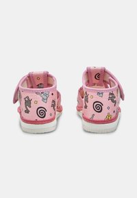 Roosa beebijalatsid loomade ja spiraalmustriga, avatud külgedega ja velcro rihmadega, nähtud seljapoolt valgel taustal.