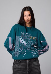 Suéter de punto color azul verdoso con un patrón geométrico en rosa y blanco, con mangas oversized y un escote redondo.