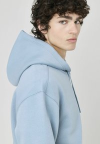 Hoodie bleu clair en tissu mélangé coton, avec capuche à cordon de serrage, poignets côtelés et coupe décontractée, au toucher lisse.