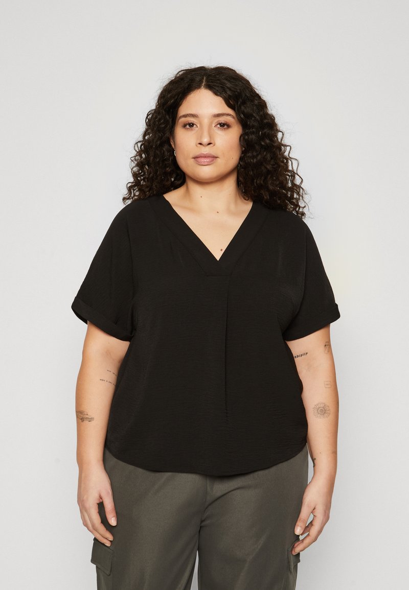 Schwarze Bluse mit V-Ausschnitt und gerollten kurzen Ärmeln, mit lockerer Passform und strukturiertem Stoff. Getragen mit grauen Cargo-Hosen.