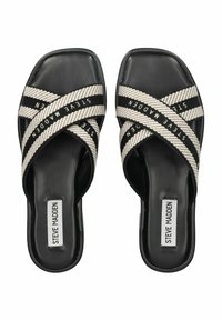 Sandales noires à semelle plate avec un orteil carré, présentant des brides tissées croisées en crème et noir, et un logo en texte noir sur les brides.