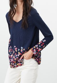 Mörkblå långärmad topp med V-ringning, med ett blommönster i rosa, gult och blått vid nederkanten och ärmarna, tillverkad av ett mjukt tyg.